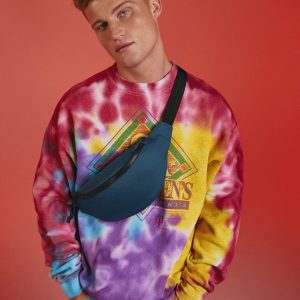 A man is standing in the image, dressed in a colorful shirt and blue bag. The background is red.