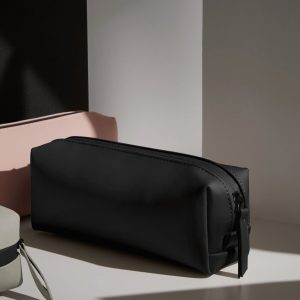 A black case is the central focus of this image, with a pink object placed on the left side. The background is composed of a white wall.