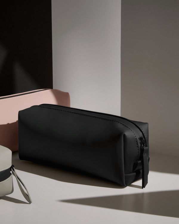 A black case is the central focus of this image, with a pink object placed on the left side. The background is composed of a white wall.