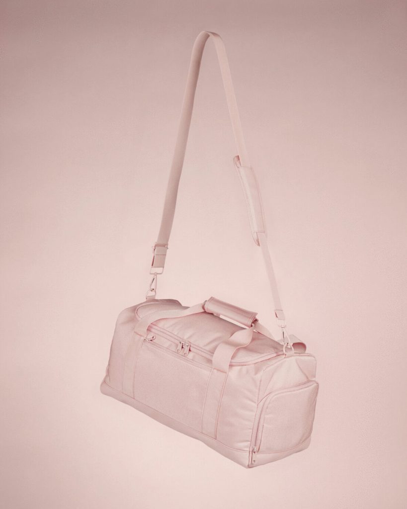 A pink-colored bag is depicted in this image, featuring a handle and a strap. The bag appears to be in motion, as if it is being carried by a person.