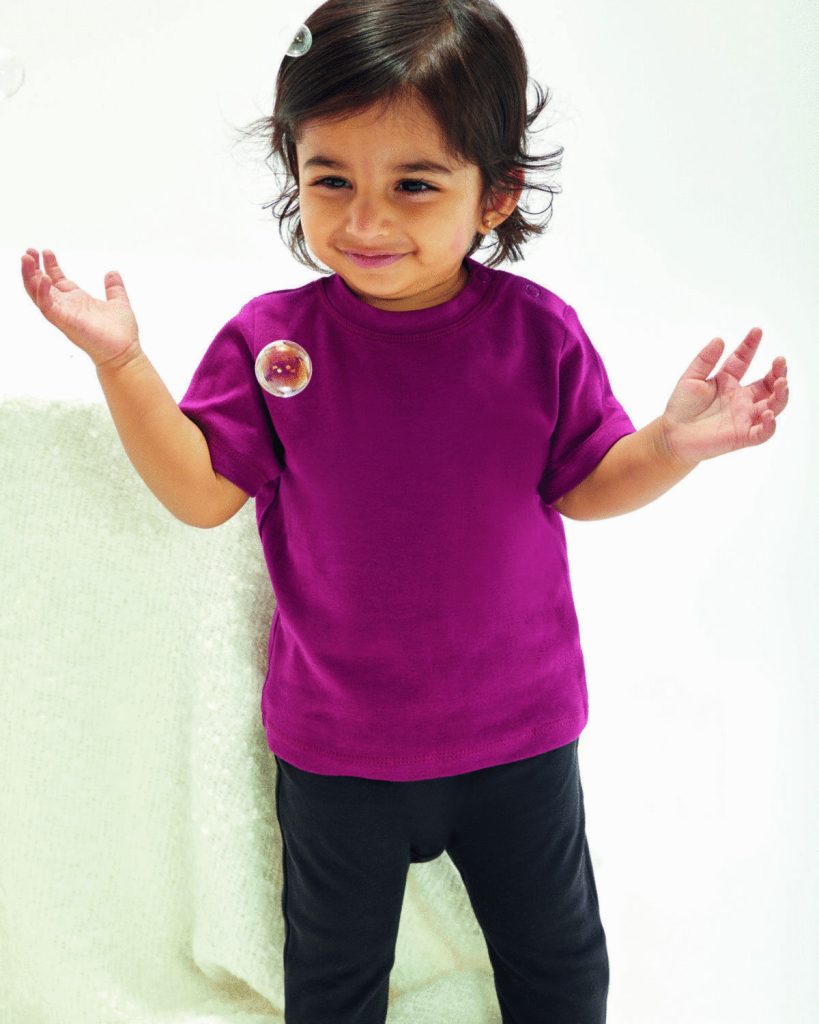 A child is standing in the image, dressed in a purple t-shirt and black pants. The background is white, and the child is smiling.