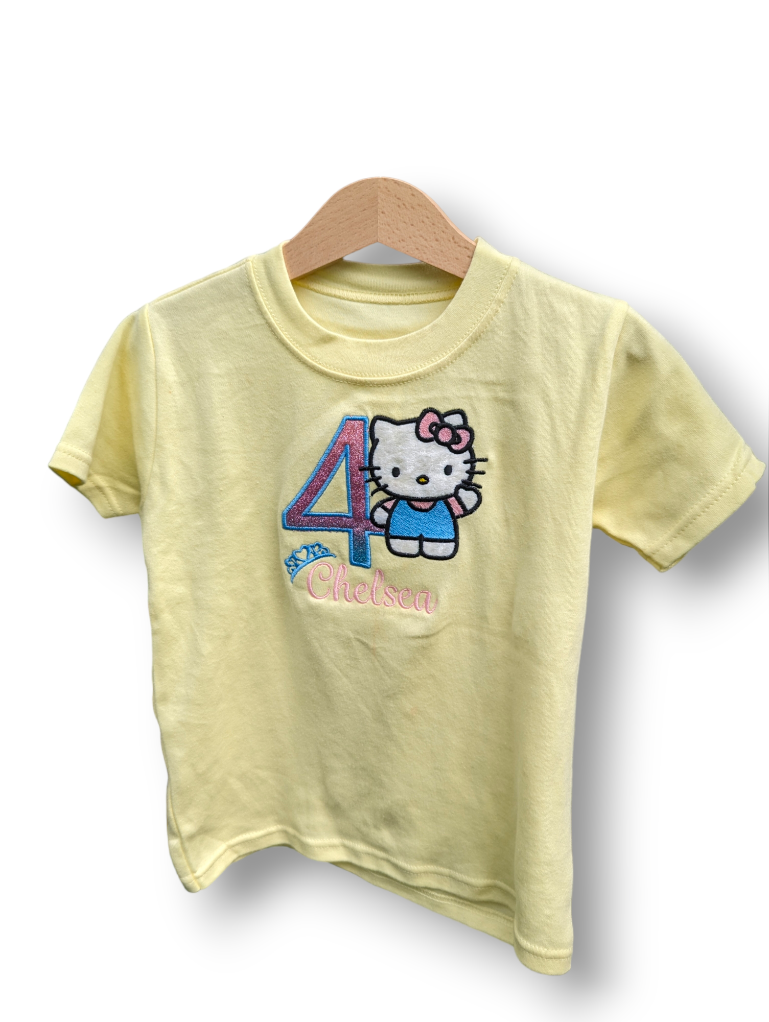 A child's t-shirt is depicted in this image, featuring a Hello Kitty design and the number four. The shirt is hanging on a hanger, and the background is white.
