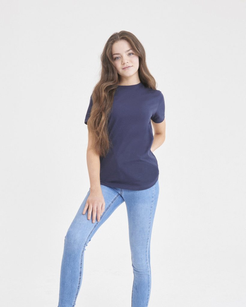 A girl is standing in the image, dressed in a blue shirt and blue jeans. The background is white, and the image appears to have been taken in a studio setting.