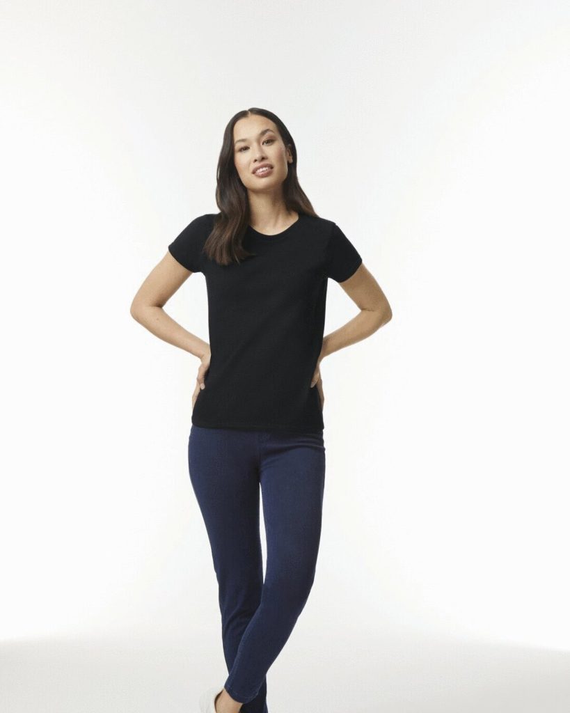 A woman is standing in the image, dressed in a black t-shirt and blue pants. She is smiling and posing for the camera. The background is white.