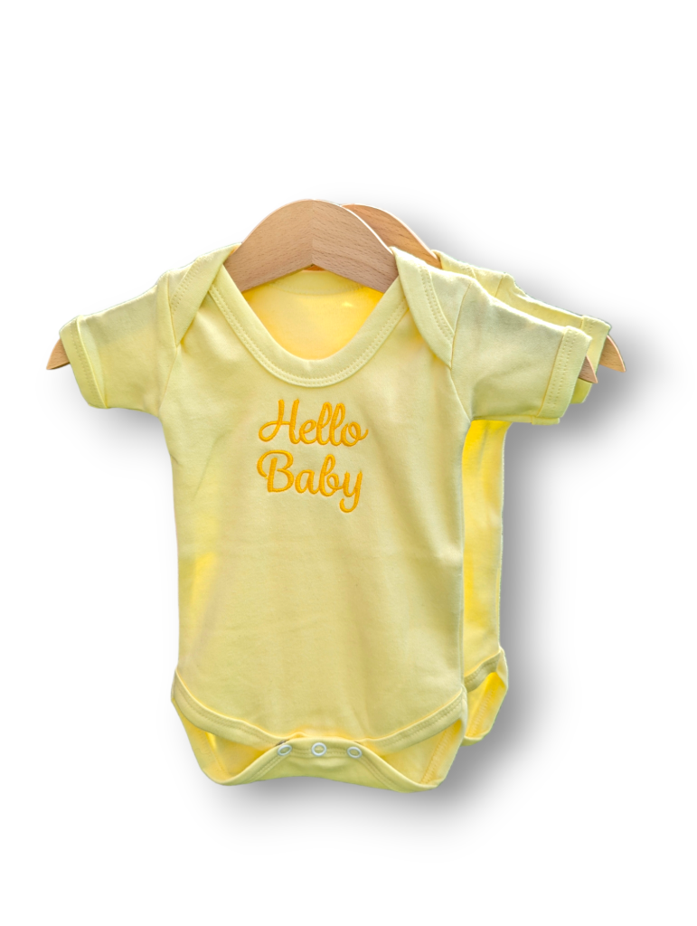 A yellow baby vest is depicted in this image, featuring the word "hello baby" written on it. The vest is hanging on a wooden hanger, and a white background is visible in the background.