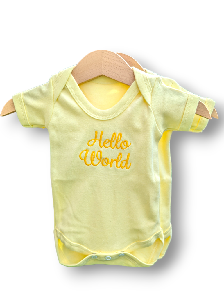 A yellow baby vest is depicted in this image, featuring the word "hello world" written on it. The vest is hanging on a wooden hanger, and the background is white.