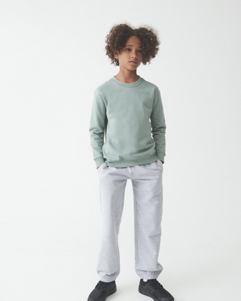 A boy is standing in the image, dressed in a grey sweat shirt and grey pants. The background is white, and the image is taken from a top-down perspective.