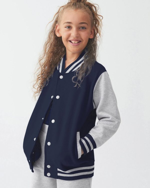 A girl is standing in the image, dressed in a blue jacket with grey stripes. She is smiling and posing for the camera. The background is white.