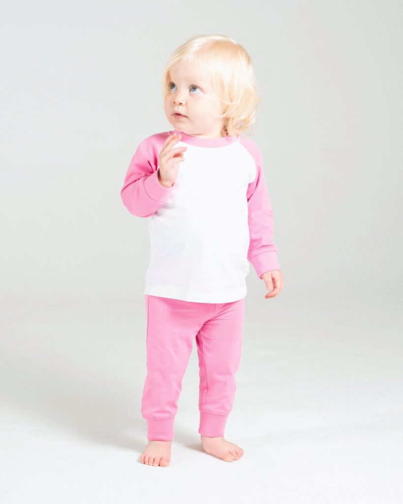 A child is standing in the image, dressed in a white and pink outfit. The background is white, and the image is taken in a studio setting.