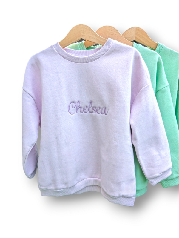 A collection of sweatshirts is displayed in this image, with the sweatshirt in the center featuring the name "Chelsea."