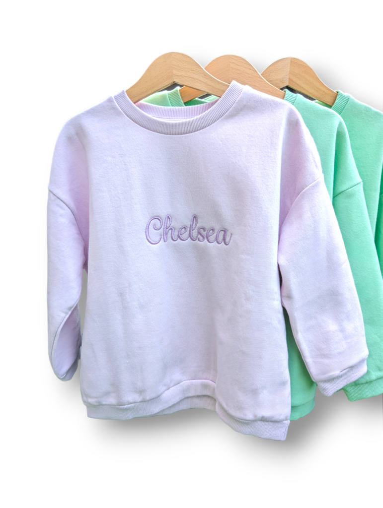 A collection of sweatshirts is displayed in this image, with the sweatshirt in the center featuring the name "chelsea. "