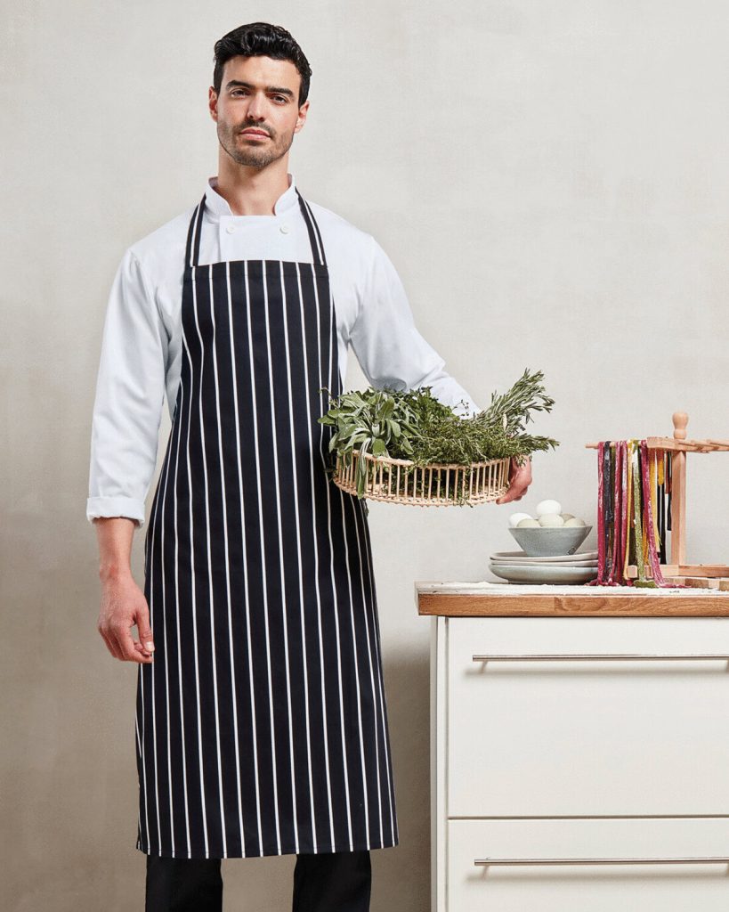 A man is standing in the image, holding a basket with plants and a bowl. The background features a wall, and a cupboard is situated to the right side of the image.