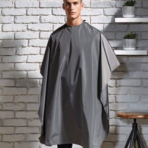 A man is standing in the image, dressed in a grey gown. The background features a brick wall, and a few potted plants are situated to the right side of the image.