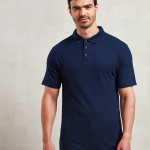 A man is standing in the image, dressed in a blue shirt and black pants. He is smiling and posing for the camera. The background is white.