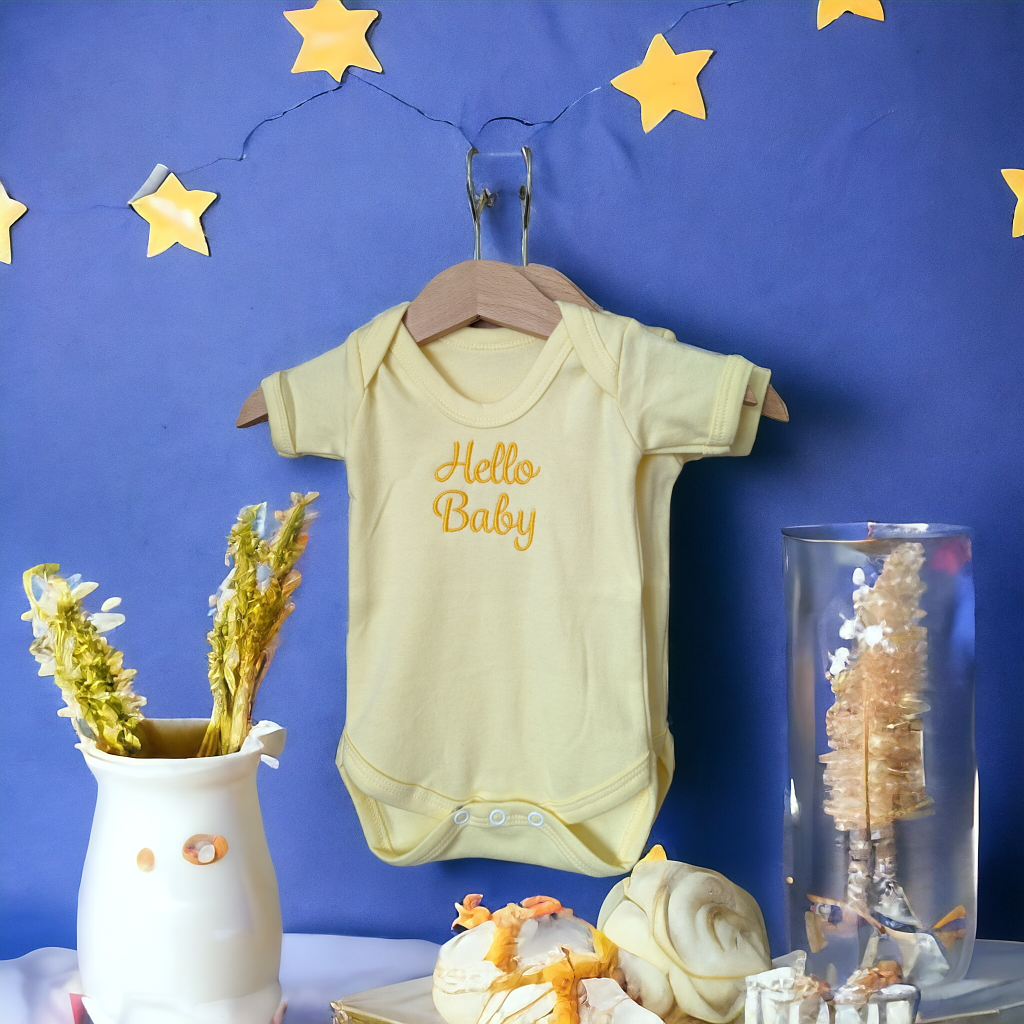 A yellow baby vest is the central focus of this image, with a white flower vase and a glass vase nearby. The background features a blue wall and a few yellow stars. The image is taken from a top-down perspective.