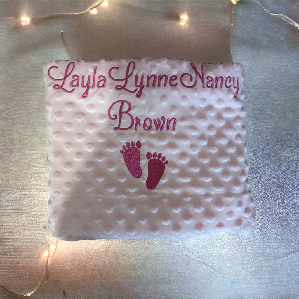 A pink blanket is depicted in this image, featuring a baby's foot and the name "layla lynn brown. " in white letters. The blanket is adorned with a few lights.