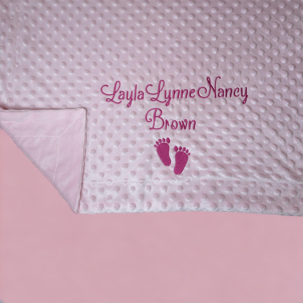 A pink blanket is depicted in this image, featuring a baby's foot and the name "Lacy Lynne Nancy Brown." Embroidered on the blanket are the names of the baby.