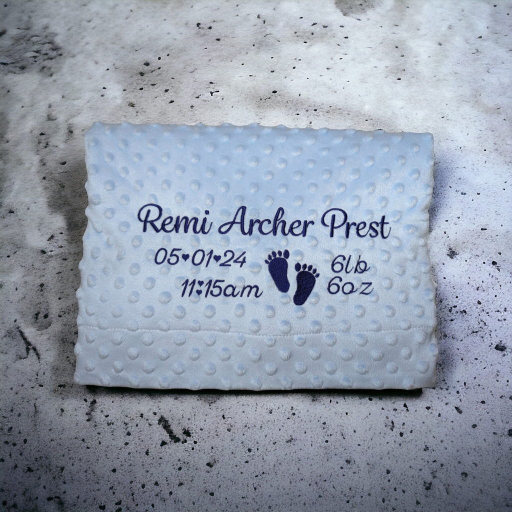 A baby blanket is depicted in this image, featuring a foot and the name "remi archer prest" written on it. The blanket is white and blue in color.