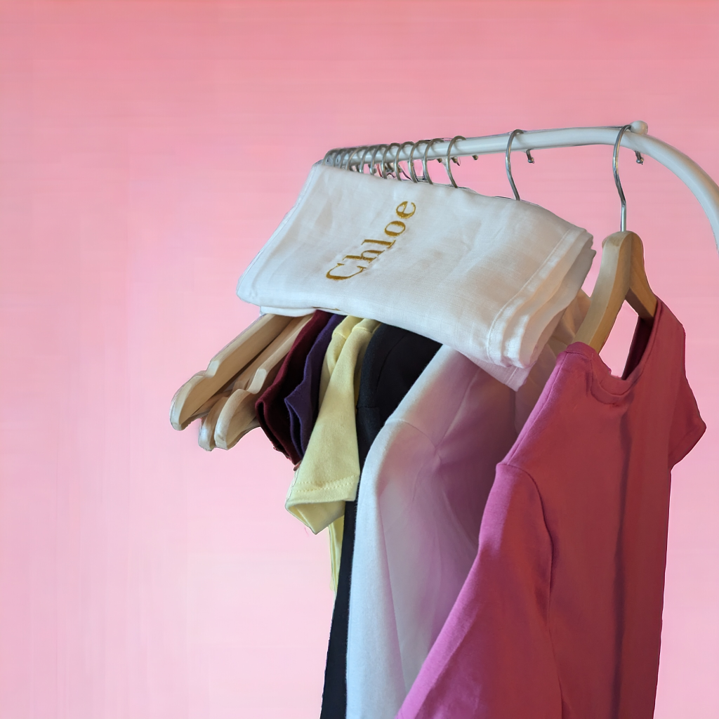 A white muslin is draped over a hanger, with a few clothes hanging from it. The background is pink.