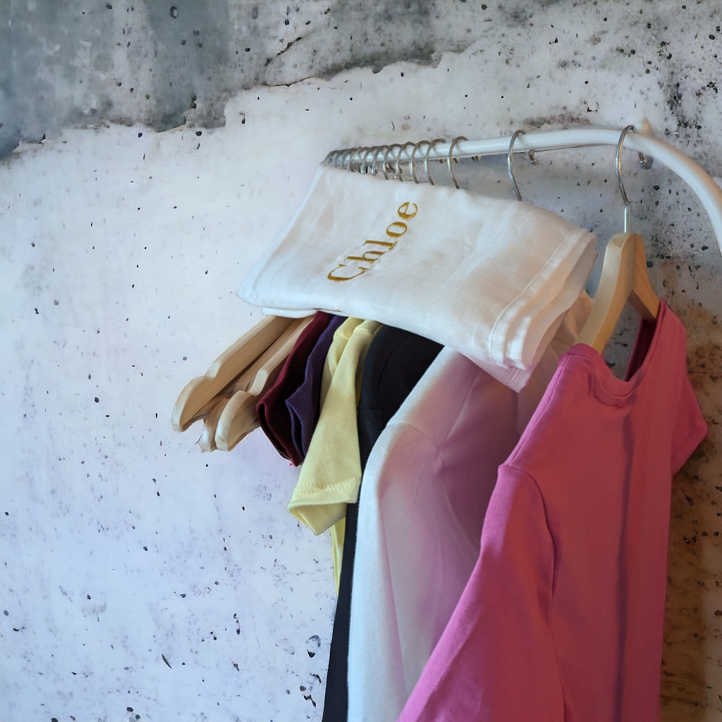 A white muslin is draped over a hanger, with a few clothes hanging from it. The background features a wall with a grey surface.