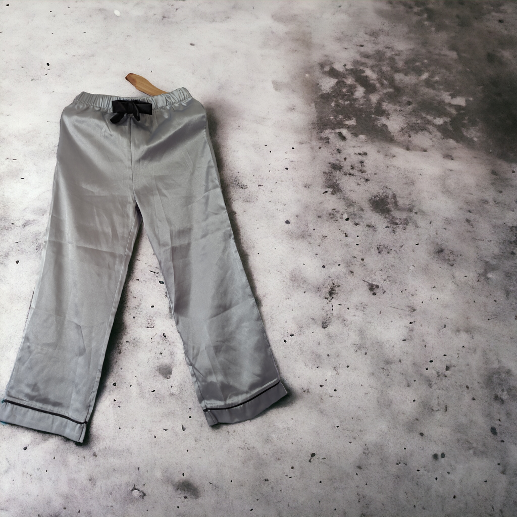 A pair of grey satin pants is depicted in this image, with a wooden hanger attached to the top. The pants are placed on a grey surface, which appears to be a floor.