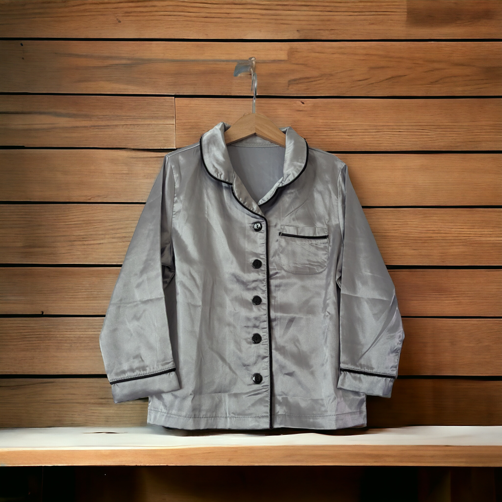 A grey satin pajama set is displayed in this image, hanging on a wooden rack. The wooden surface is visible in the background, along with a wooden wall.