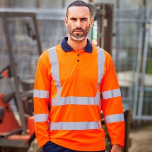 A man is standing in the image, dressed in an orange shirt and blue pants. The background features a forklift, a fence, and a building.