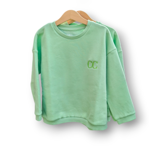A child's sweatshirt is depicted in this image, featuring a green color and the letters "CC" embroidered on it. The sweatshirt is hanging on a hanger, and a white background is visible.