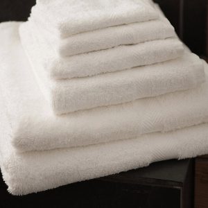 A collection of white towels is arranged on a black surface, with a sink visible in the background. The image is taken from a close perspective, focusing on the towels.