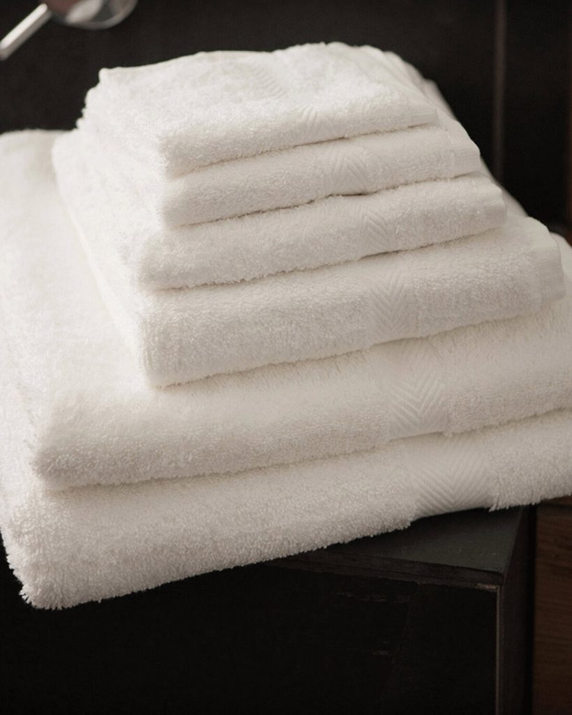 A collection of white towels is arranged on a black surface, with a sink visible in the background. The image is taken from a close perspective, focusing on the towels.