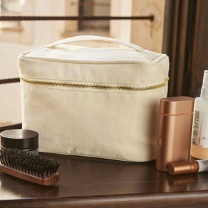 A white vanity case is the central focus of this image, with a brush and other items placed on top. The background features a wall, window, and a door.