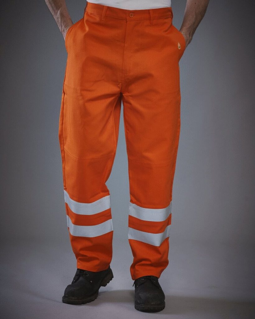 A man is standing in the image, dressed in orange pants with reflective flame retardant. The pants have a reflective strip on the inside, and the background is white.