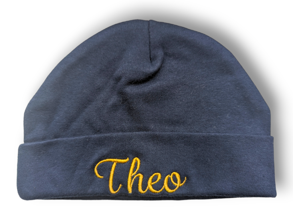 A black beanie hat is the central focus of this image, with the word "theo" embroidered on it. The background is white.