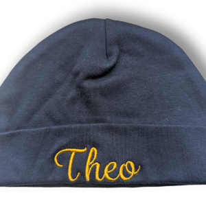 A black beanie hat is the central focus of this image, with the word "THEO" embroidered on it. The background is white.