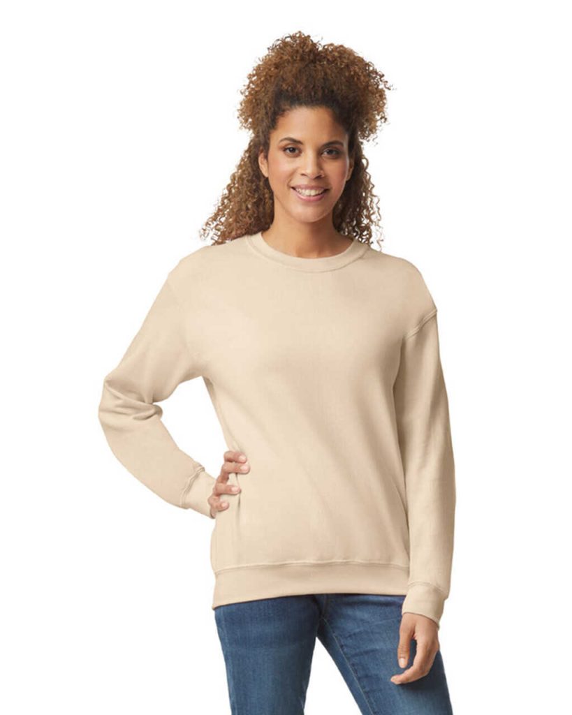 A woman is standing and smiling in the image, dressed in a cream-colored sweatshirt. The background is white.