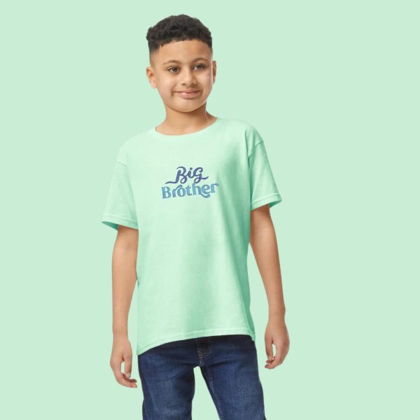A boy is standing in the image, dressed in a green T-shirt with the words "Big Brother" written on it. The background is white.