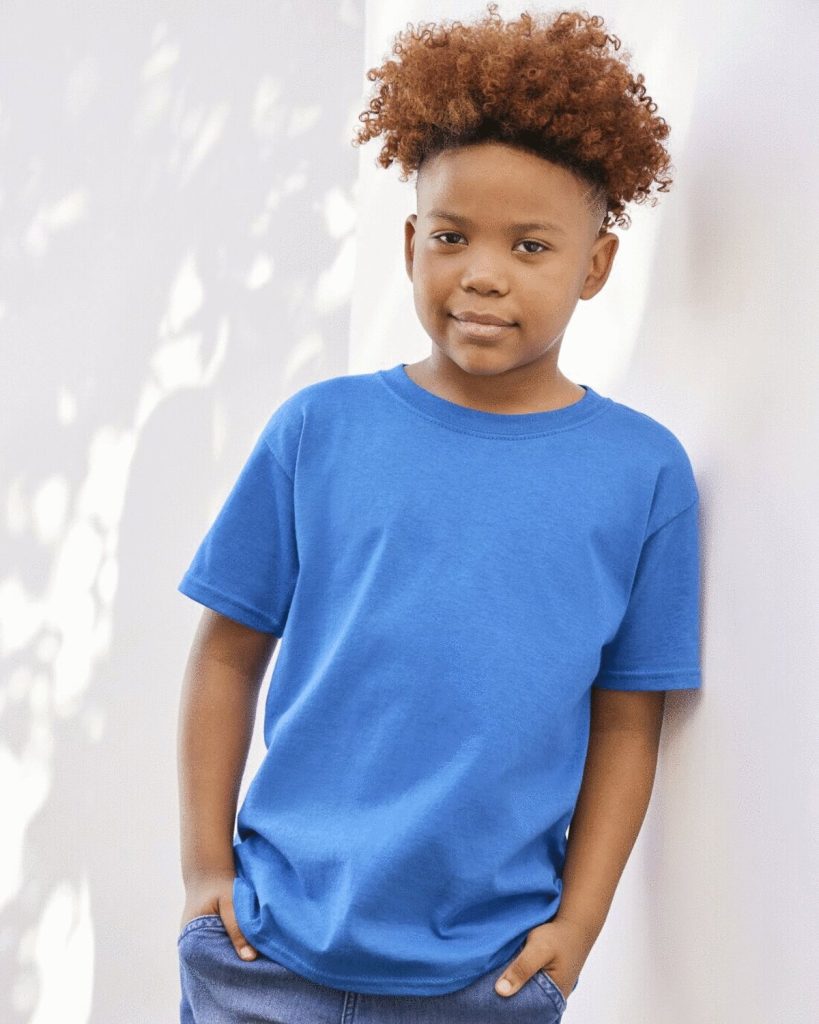 A boy is standing in the image, dressed in a blue t-shirt. The background features a white wall, and a tree can be seen in the top left corner.