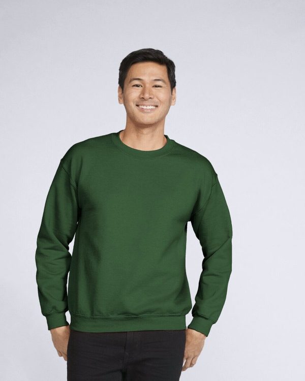 A man is standing and smiling in the image, dressed in a green sweatshirt. The background is white.
