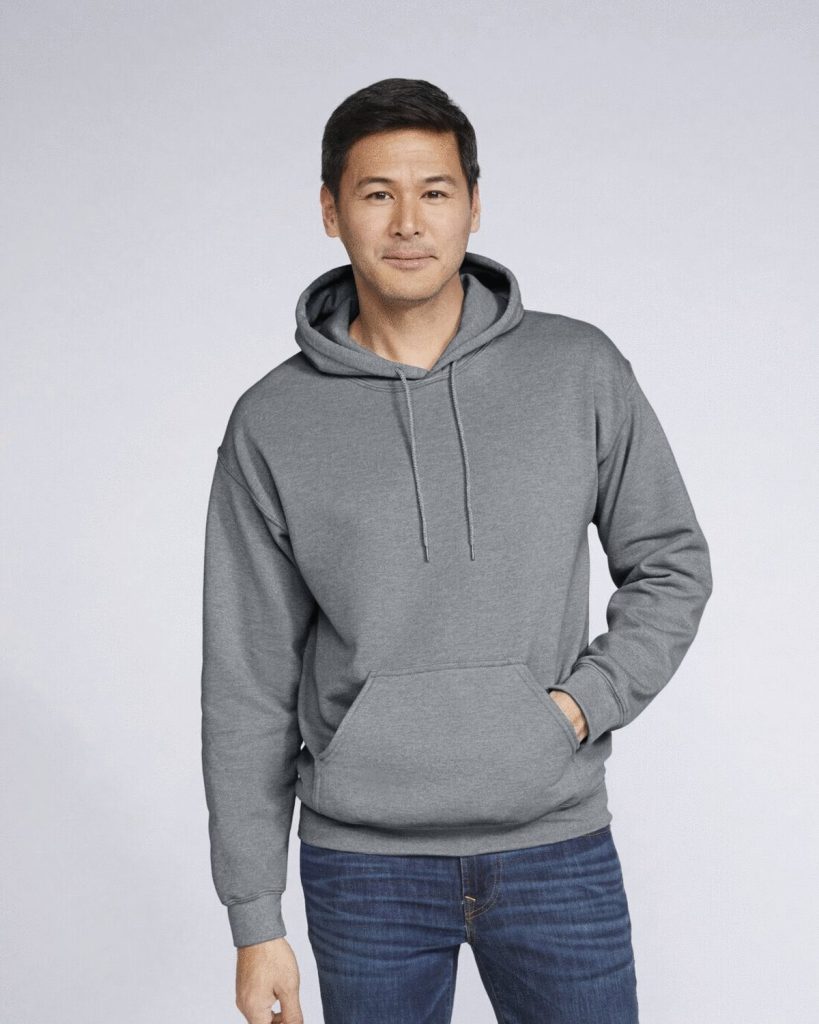 A man is standing in the image, dressed in a grey hooded sweatshirt. The background is white, and the image appears to have been taken in a dimly lit environment.