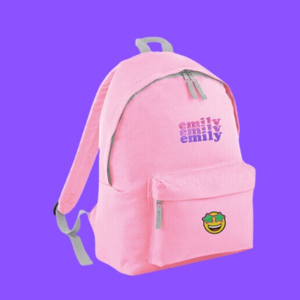 A pink backpack is the central focus of this image, with text written on it in purple and pink. The background is a light blue color.