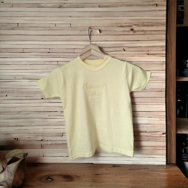 A yellow t-shirt is displayed in the image, featuring the word "Summer" written in white letters. The shirt is hanging on a hanger, and a wooden wall is visible in the background.