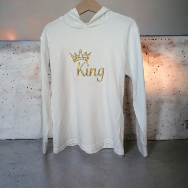A white hoodie is displayed in the image, featuring a crown design. The hoodie is hanging on a wooden rod, with a light source visible behind it.