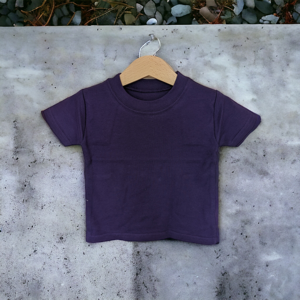 A child's purple t-shirt is displayed in the image, hanging on a wooden hanger. The background features a stone wall.