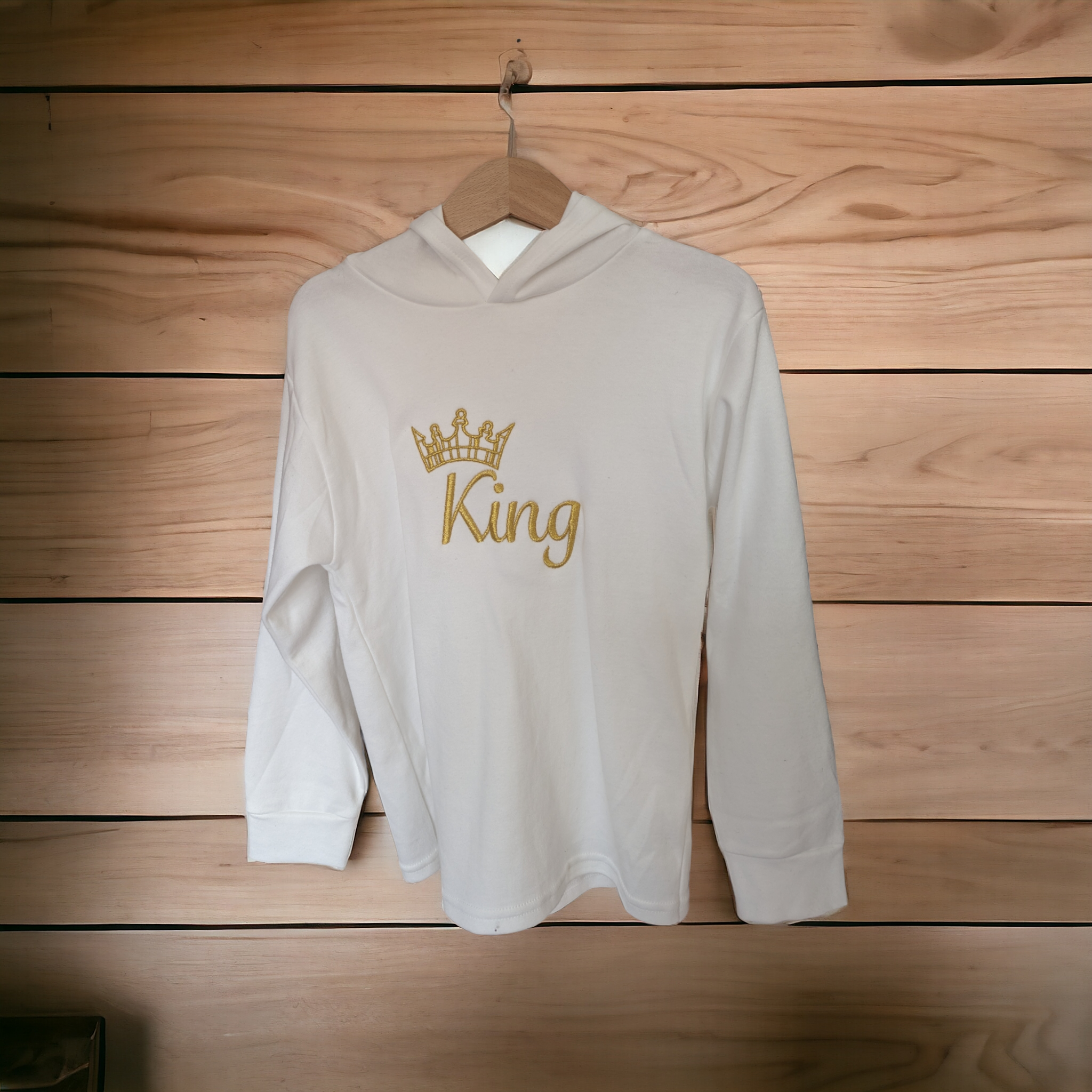 A hoody is displayed in the image, featuring a crown design. The hoody is hanging on a wooden surface, which appears to be a wall.