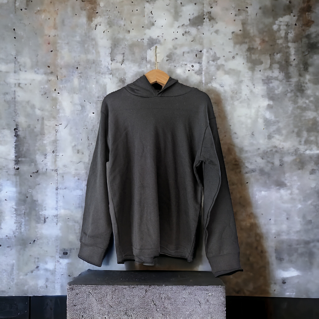 A hoodie is displayed in the image, hanging on a wooden rod. The background features a wall, and a stone is situated at the bottom of the image.