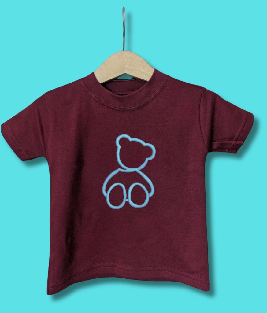 A maroon-colored t-shirt is displayed in the image, featuring a teddy bear image in blue and white. The teddy bear is depicted in a standing position, with a blue background.