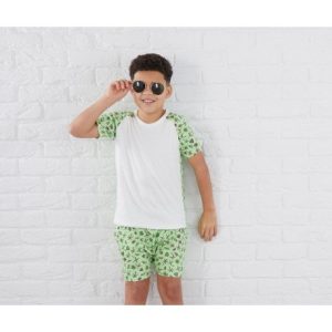 A boy is standing in the image, wearing a white t-shirt and green shorts with a design of palm trees. The background features a white wall.