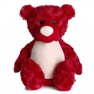 A red-colored teddy bear is depicted in this image, with a white and cream color design on its face. The background is white, and the image appears to have been taken in a dimly lit environment.