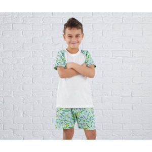 A boy is standing in the image, dressed in a white t-shirt and green shorts. The background features a white brick wall.