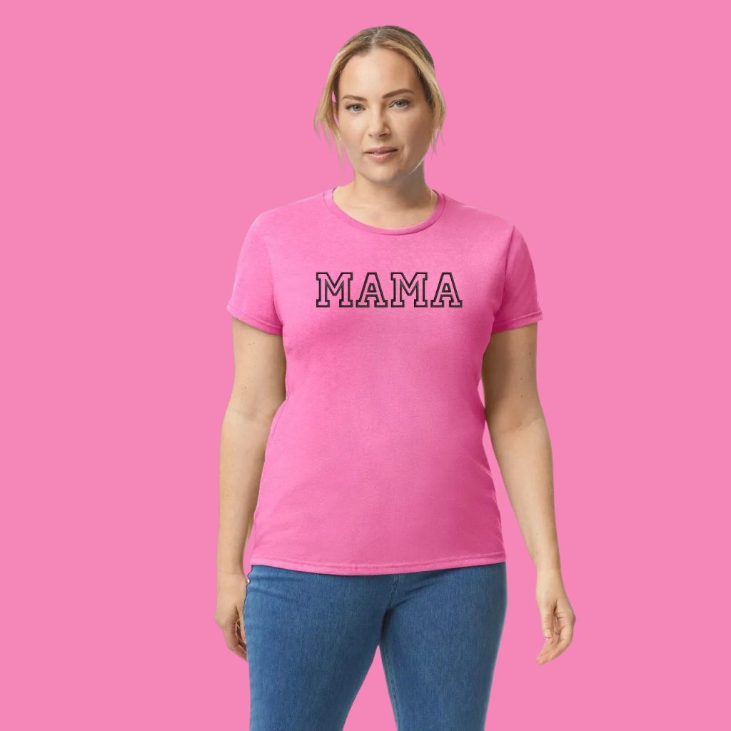 A woman is standing in the image, dressed in a pink t-shirt with the word "mama" written on it. The background is pink.